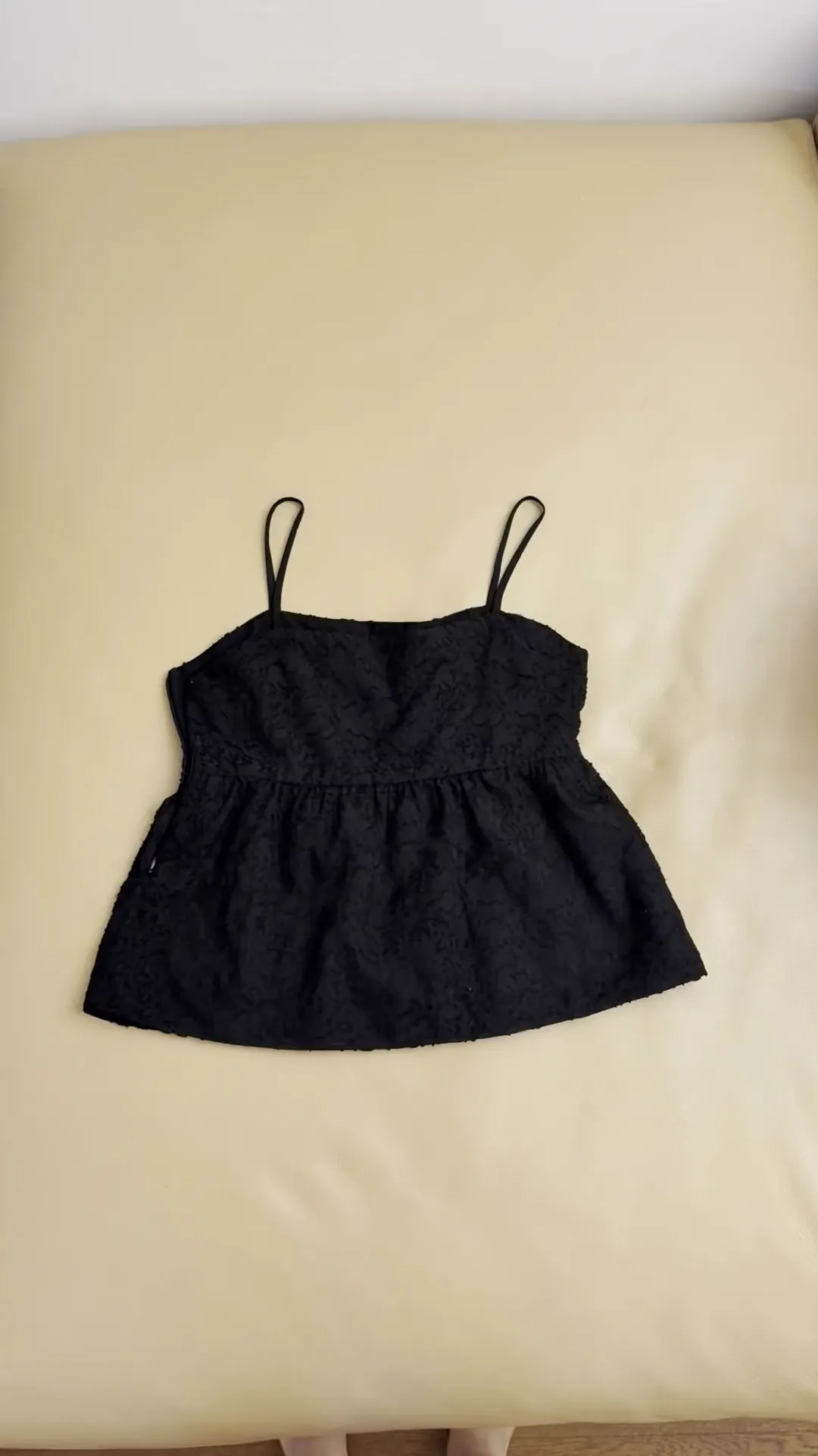 Real footage of a black lace camisole being laid flat and photographed, inside the camera's capture frame.